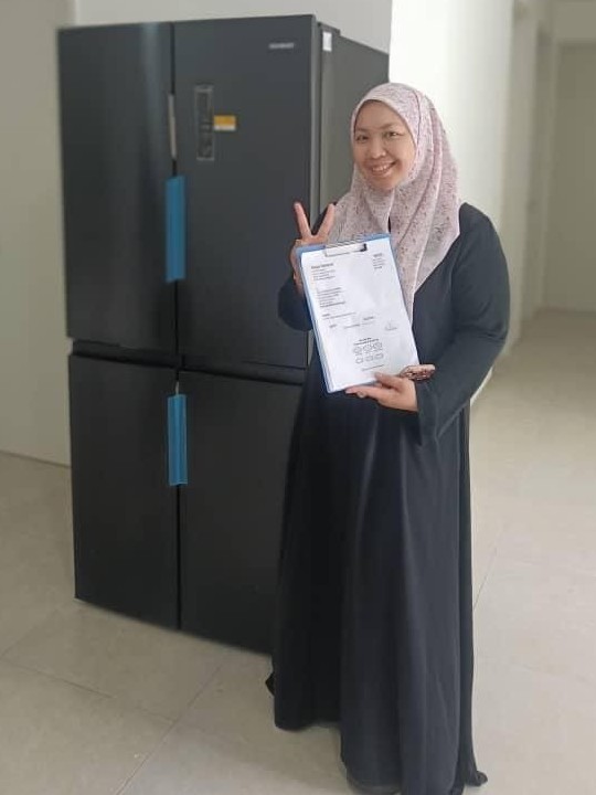 Pelanggan tersenyum memegang borang penerimaan di hadapan peti sejuk 4 pintu