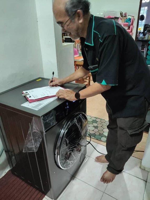 Pelanggan tersenyum menandatangani borang penerimaan di atas mesin basuh